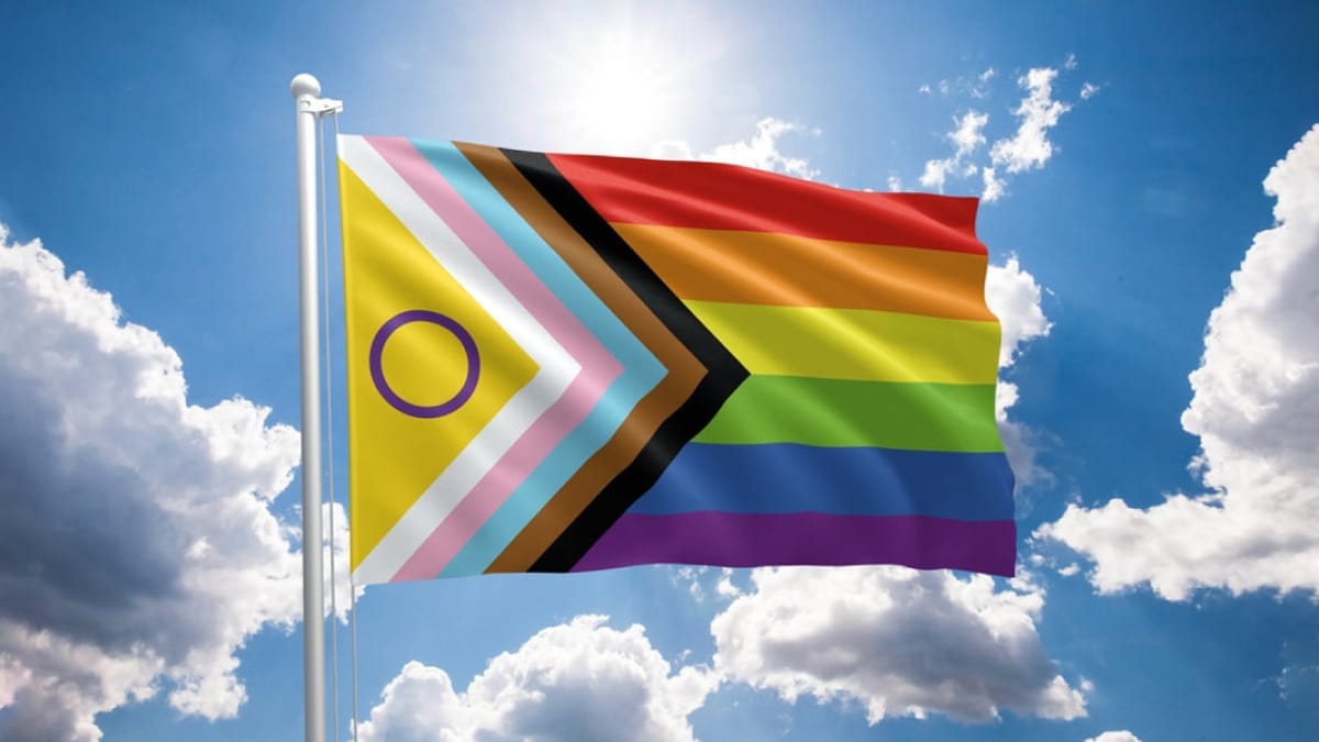 A LGBTQI+ flag waving with a cloud background